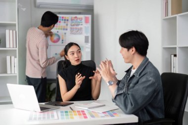 Modern bir çalışma alanında, bir grafik tasarımcı renk şemaları ve tasarım stratejileri üzerine ilgi çekici bir tartışmayı kolaylaştıran fikirleri meslektaşlarıyla paylaşır. Bu ayar takım çalışmasını ve yeniliği teşvik eder.