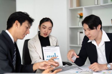 Bir iş ekibi anahtar ölçüler ve içgörüleri tartışmak üzere masanın etrafında toplanırken, görsel veri temsilini gözden geçirir, işbirliği ve yeniliği teşvik eder.