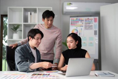 Çağdaş bir ofis alanında, iki takım arkadaşı bir dizüstü bilgisayarda tasarım seçeneklerini gözden geçirir, açık tartışmaları ve projelerini rafine ederken görsel paylaşımı teşvik ederler..