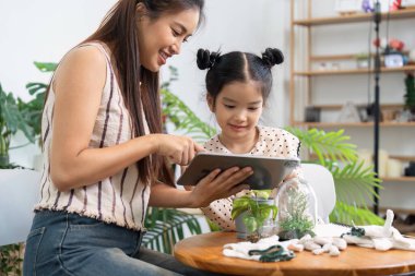 Bir anne ve kızın evdeki bahçe işleriyle teknolojiyi harmanlayan bir tablette bitki bakımı talimatlarını inceledikleri büyüleyici bir sahne..