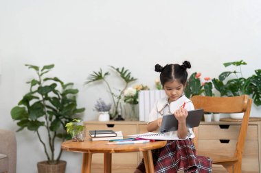 Meraklı bir kız okul gereçleri ve bitkilerle çevrili defterini inceliyor ve önümüzdeki okul yılına hazırlanırken öğrenme hevesini gösteriyor..