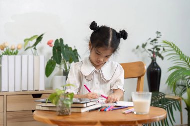 Elinde parlak işaretlerle, çocuk defterine yazıyor, okula hazırlanırken yaratıcılığını ve bağlılığını gösteriyor..