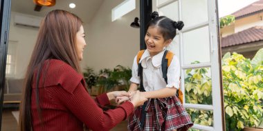 Işıl ışıl gülümseyen küçük kız annesinin elini tutuyor. Okuldaki ilk günü için heyecanını yansıtıyor. Etrafı güzel bir ev ortamıyla çevrili..