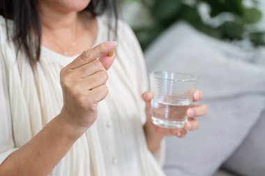 Yaşlı bir kadın vitaminlerini bir bardak suyun yanında tutuyor. Bu da günlük sağlık durumunun sağlık bakımına ve uygun ilaçlara odaklandığını gösteriyor..