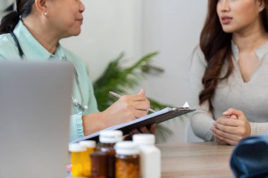 Yaşlı bir doktor hastasını aktif olarak dinler, hastanın refahına odaklanmış dostane bir konsültasyonda önemli ayrıntıları not eder..