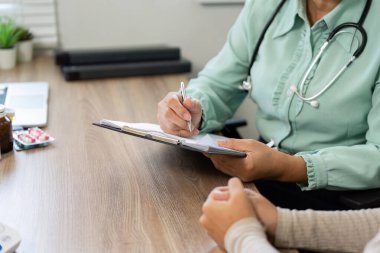 Yaşlı bir doktor, bir hastaya danışmanlık yaparken dikkatlice panoya yazarak, klinik bir ortamda kişiselleştirilmiş tedavinin önemini gösteriyor..