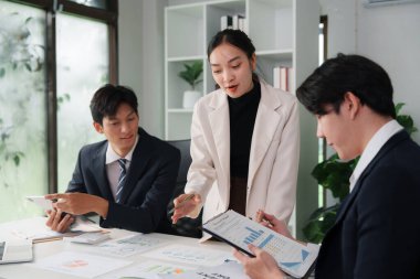 Modern bir ofis ortamında, bir iş kadını iş arkadaşlarıyla etkin bir strateji oluşturmak için çizelgeleri ve verileri gözden geçirir..