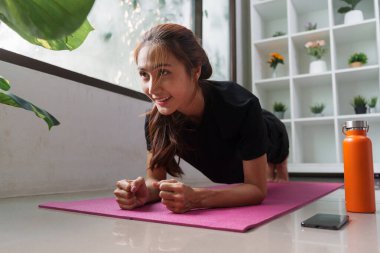 Çekirdeğini güçlendirmeye odaklanan bir kadın, yoga minderinin üzerinde kalas pozisyonu alır ve fitness yolculuğuna kendini adadığını gösterir..
