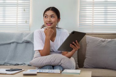 Neşeli genç bir kadın koltuğunda tabletine sarılıyor, görevlerini yaparken evin esnekliğinin ve rahatlığının tadını çıkarıyor..