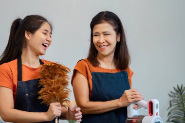 Neşeli bir anne ve kız, aydınlık oturma odalarında bir süpürge ve süpürge tutarken gülümseyen ve gülen neşeli bir anı paylaşırlar..