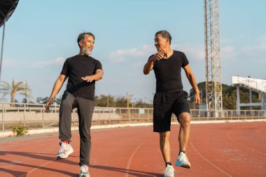 Açık havada egzersiz yapan iki kıdemli insan, refahı ve aktif yaşamı destekleyen bir toplum ortamında destekliyor..