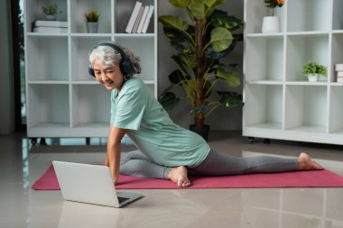 Evde yoga yapan yaşlı bir kadın, yaşlıları iyileştiriyor ve çevrimiçi rehberlikle aktif bir yaşam sürüyor..