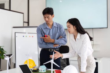 Çalışma alanındaki iki mühendis, sürdürülebilirlik ve yenilikçi mimari fikirler üzerine projelerini tartışarak konut modellerini analiz ediyorlar..