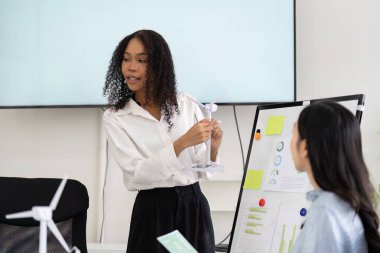 Tutkulu bir iş adamı, sürdürülebilir uygulamalar ve ESG girişimleri hakkında görüşlerini paylaşıyor, noktalarını göstermek için bir rüzgar türbini modeli kullanıyor.