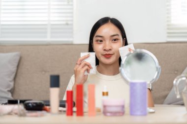 Genç bir kadın makyaj ürünlerini elinde tutuyor. Güzellik rutiniyle, kendine güveni ve kendine güveni tamken gülümsüyor..