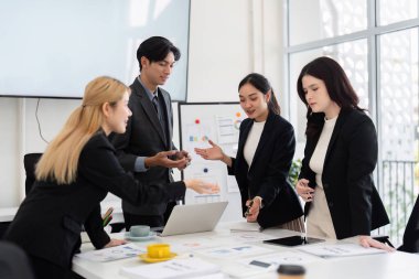 İş dünyasından çeşitli uzmanlar bir toplantı sırasında işbirliği yaparak, stratejileri tartışıyor ve parlak bir ofis ortamında dizüstü bilgisayarın etrafında görüşlerini paylaşıyorlar..