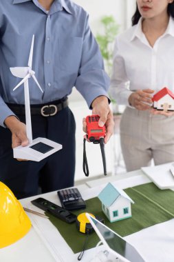 Bir mühendis, gelecekteki projeler için yenilikçi sürdürülebilir teknolojiyi vurgulayarak bir meslektaşına bir rüzgar türbini modeli ve çeşitli inşaat unsurları sunuyor..