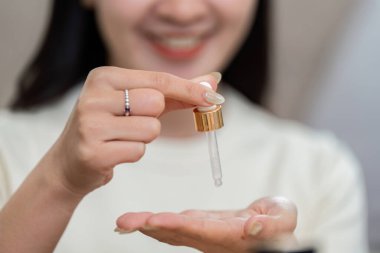 Gülümseyerek, bir kadın eline serum sürer, doğal güzelliğini ve kendine olan güvenini güçlendirmede cilt bakımının önemini vurgular..