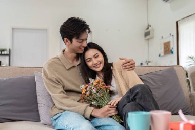 Kanepede oturan neşeli bir çift, sıcak bir oturma odasında bir buket çiçekle sevgi dolu bir anı paylaşıyorlar..