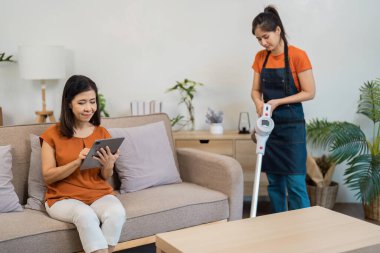 Temizlikçi, modern bir oturma odasını süpürgeyle etkin bir şekilde temizler. Profesyonel ev temizleme hizmetlerinin rahatlığını ve rahatlığını vurgular..