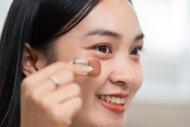 Gülümseyen bir kadın bronzlaştırıcı sürer, özelliklerini vurgular ve mutluluk saçar, güzellik rutininden gelen güçlü hissi güçlendirir..