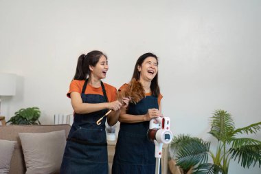 İki kadın oturma odasını modern aletlerle temizlemekten mutlu olurlar. Takım çalışması ve temiz, rahat bir ortam..