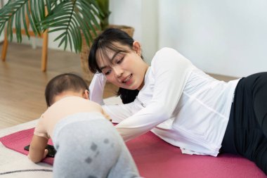 Antrenman minderinde rahatça uzanan bir anne, bebeğiyle etkileşime girer. Hem sporun uygunluğunu hem de eğlencesini vurgular. Paylaştıkları eşsiz bağı vurgular..