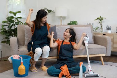 Neşeli bir anne ve kız, temizlik aletleri ve malzemelerle çevrili oturma odalarında başarılı bir temizlik oturumunu kutluyorlar..