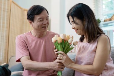 Neşeli bir son sınıf çifti çiçeklerle hassas bir anı paylaşıyor, sıcak ve sıcak bir evde sevgililer gününü kutluyor..