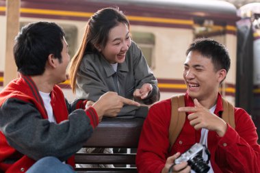 Tren istasyonunda eğlenceli bir sohbete giren üç arkadaş, trenlerini beklerken hikayelerini ve kahkahalarını paylaşıyorlar. Bu görüntü yoldaşlığın ve seyahatin heyecanını yakalar..