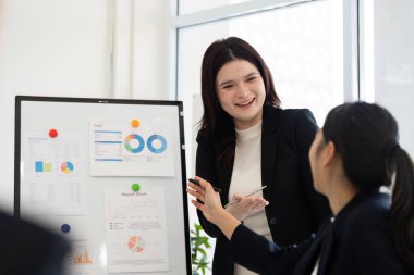 Hareketli bir ofiste, profesyonel bir kadın verileri coşkuyla sunarak tartışmayı yönetirken, meslektaşları da görüşlerini ve görüşlerini sunuyor. Takım çalışması ön planda..