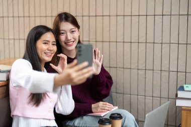 İki arkadaş, akademik yolculuklarını kutlamak için kitap ve çalışma materyalleriyle çevrili, neşeli bir selfie çekerken koleje dönüş ruhunu kucaklıyor..