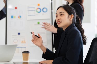 Profesyonel bir kadın modern ofis ortamında canlı bir tartışmaya katkıda bulunur, görüşlerini paylaşırken meslektaşları onun fikirleriyle ilgilenir, takım çalışmasını teşvik eder..