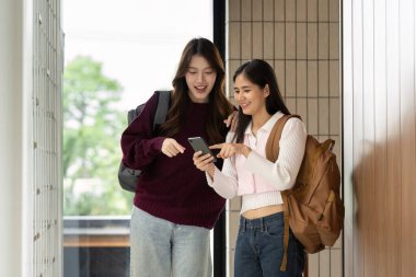 İki üniversiteli arkadaş neşeli bir kampüs ortamında telefona bakarken sohbet ve kahkahalarla eğleniyorlar..