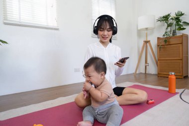 Bir anne, kulaklıklarla spor yapmayı sever. Yoga minderinde oynarken meraklı bebeğine göz kulak olur. Aile zamanının keyfini artırır..