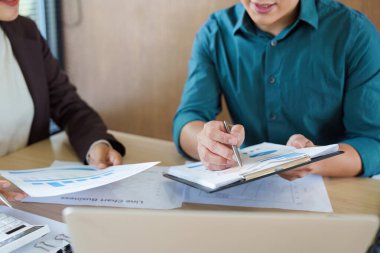 İki profesyonel, bir erkek ve bir kadın, bir toplantıda proje çizelgeleri ve mali raporları tartışıyorlar, takım çalışmasını ve stratejik planlamayı vurguluyorlar..