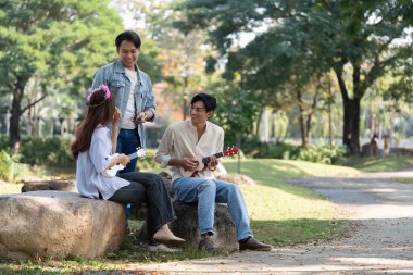 Üç arkadaş açık havada güneşli bir günün tadını çıkarıyorlar, birlikte ukulele çalıyorlar, doğadaki neşeyi, yaratıcılığı ve değerli anları kutluyorlar..