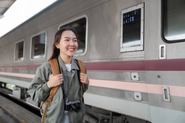 Neşeli bir gezgin, yaklaşan macerasına hazırlanırken platformda gülümsüyor. Arka plandaki klasik tren nostaljik atmosfere ekleniyor..