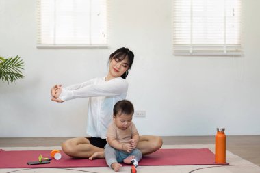 Kendini adamış bir anne, evde yoga seansı, dengeleyici sağlık ve annelik süresince, küçük çocuğunun paspasın üzerinde oyuncaklarla oynaması, aile refahının önemini gözler önüne seriyor..