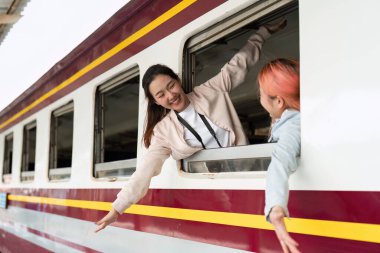 Heyecanlı arkadaşlar birbirlerini trenden selamlar, neşe ve bağlantı anlarını yakalarlar. Gülüşleri seyahat ve arkadaşlığın mutluluğunu yansıtıyor..