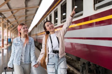Tren istasyonunda iki genç kadın, biri selfie çekerken diğeri gülümsüyor, ikisi de maceralı bir yolculuk deneyimi için hazır..