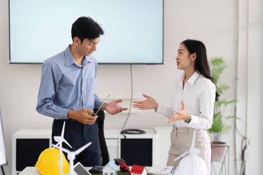 Modern bir çalışma alanında, mühendislerden oluşan bir ekip fikir üretmek için detaylı modeller kullanarak sürdürülebilir yapı tasarımları üzerinde fikir alışverişinde bulunuyor..