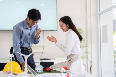 Parlak bir ofiste, iki mühendis hevesle çevre dostu inşaat projelerinde işbirliği yapıyor, modellerini sergiliyor ve sürdürülebilirlik için yenilikçi fikirler üretiyorlar..