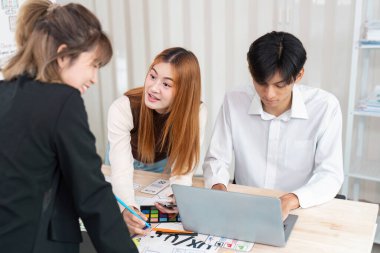 Üç yaratıcı UI UX fikirleri hakkında dinamik bir diyalog içine girerek, bir dizüstü bilgisayar ve renkli tasarım araçları kullanarak birlikte projeler oluştururlar..