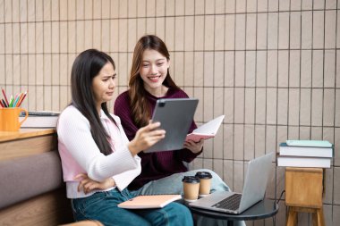 İki öğrenci, bir tablet üzerinde bir projeyi incelerken, kahve eşliğinde, akademik yaşam süresince takım çalışmasının ve öğrenim molalarının önemini vurgulayarak görüşlerini paylaşıyor..