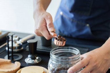 Barista, gıda ve içecek endüstrisinde sürdürülebilirliğe doğru kaymayı vurgulayarak, doğru miktarda organik kahve çekirdeği seçmek için bir ölçüm kaşığı kullanıyor..