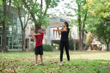 Bir anne ve oğul, güzel bir park ortamında hafif esneme egzersizleri yapar, sağlık ve aile bağlarını paylaşımlı fiziksel aktivitelerle desteklerler..