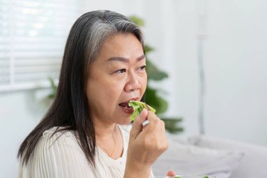 Olgun bir bayan, sağlığının ve sağlığının önemli bir unsuru olarak dikkatli bir şekilde yemenin önemini yansıtarak yemeğinin tadını çıkarır..