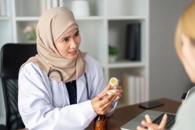 Sıcak bir klinik ortamında, bir sağlık hizmetleri sağlayıcısı bir hastayla ilaçları hakkında temas kurar, tedavi planına anlayış ve uyumu teşvik eder..