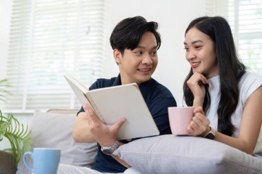 Genç bir çift birlikte oturur, kitap okurken kahkahalarını ve bağlantılarını paylaşır ve sıcak oturma odalarında kahvelerini yudumlarlar..